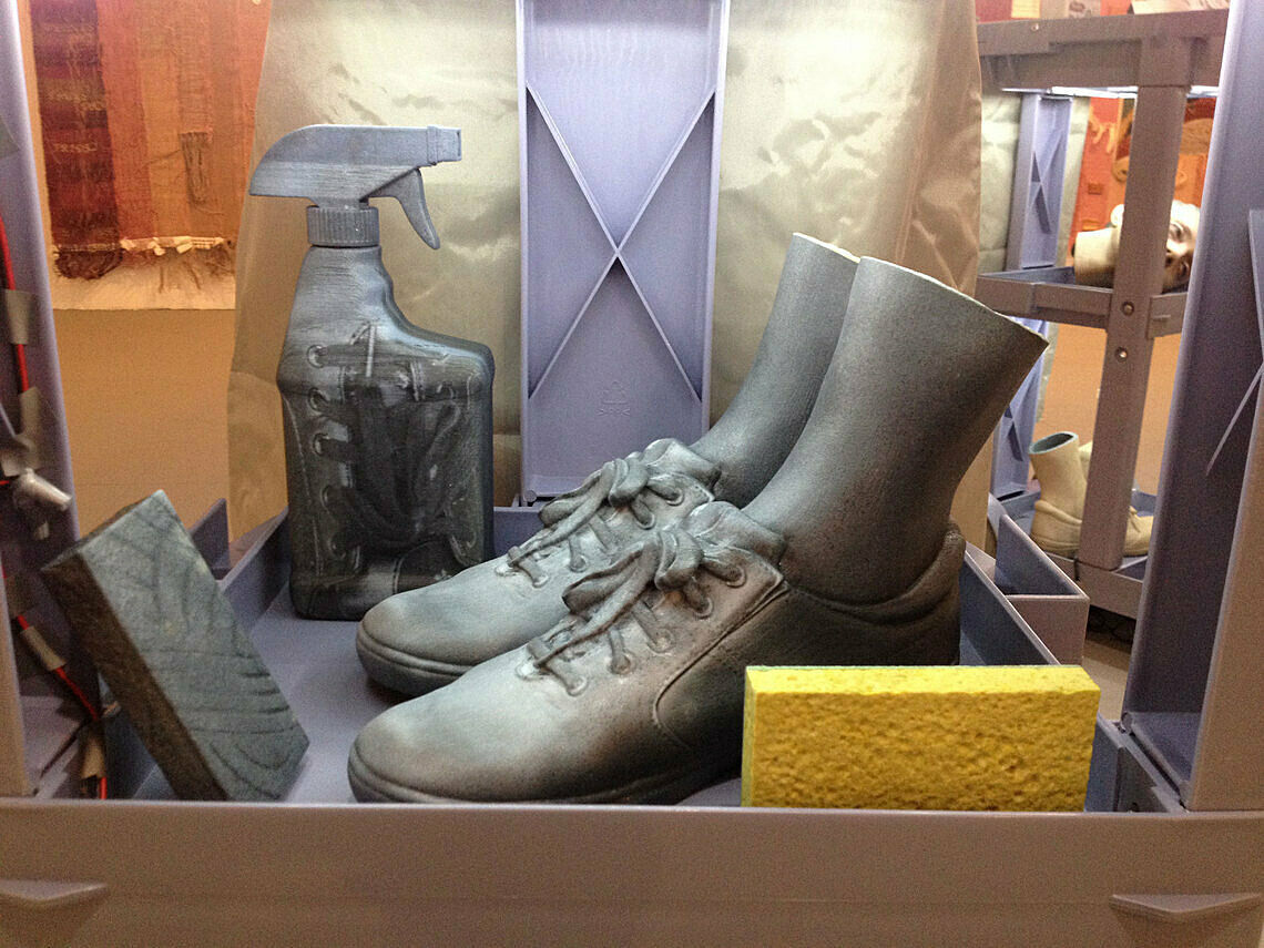A sculpture of a pair of shoes with ankles protruding from them lies among common cleaning tools.