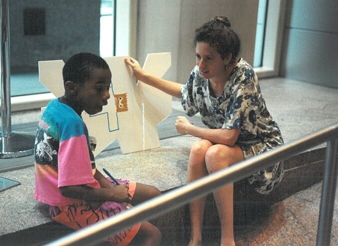 A Whitney Museum intern talks to a student while holding an artwork.