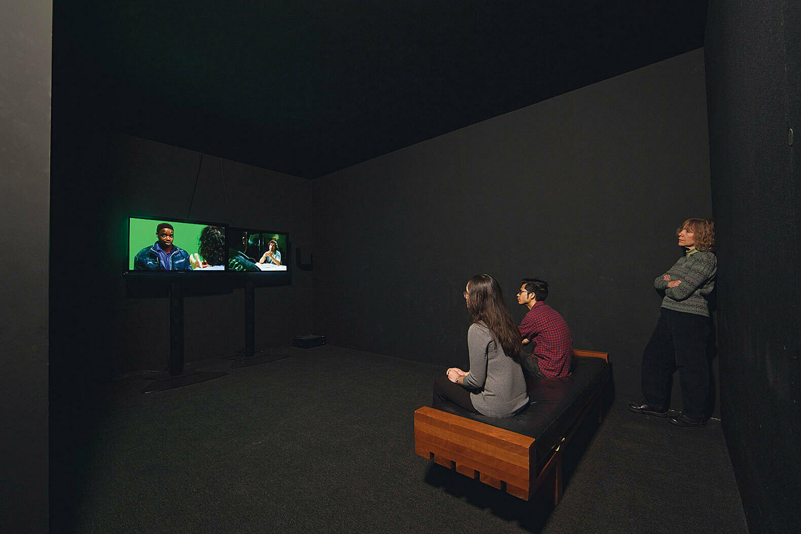 Visitors watching an Omer Fast video in a dark room