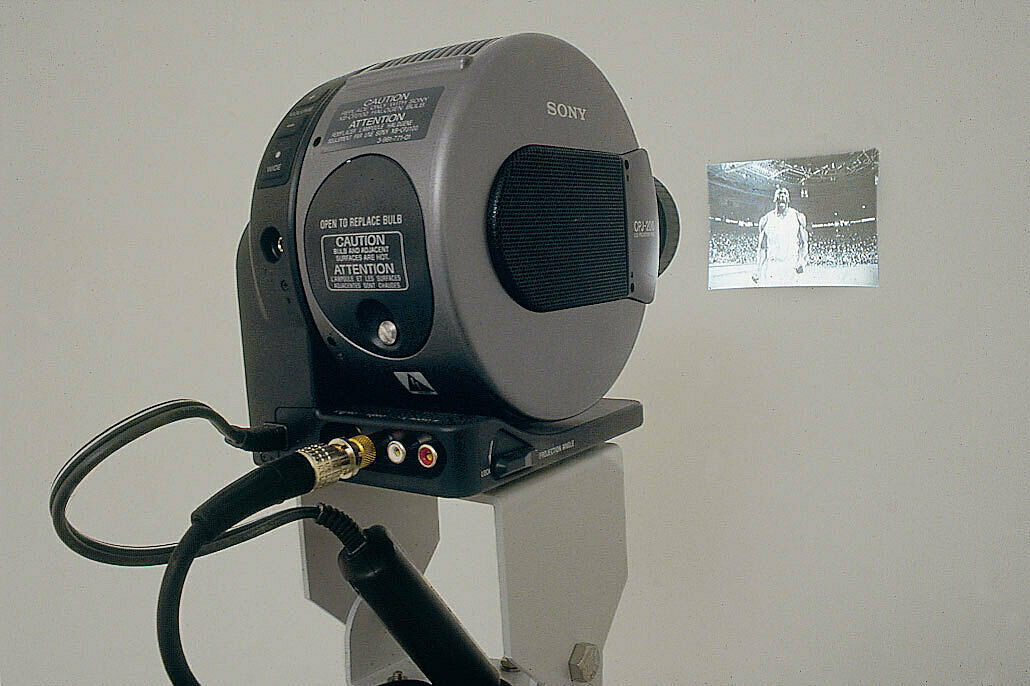 A projector close to a wall, casting a tiny image of a basketball player