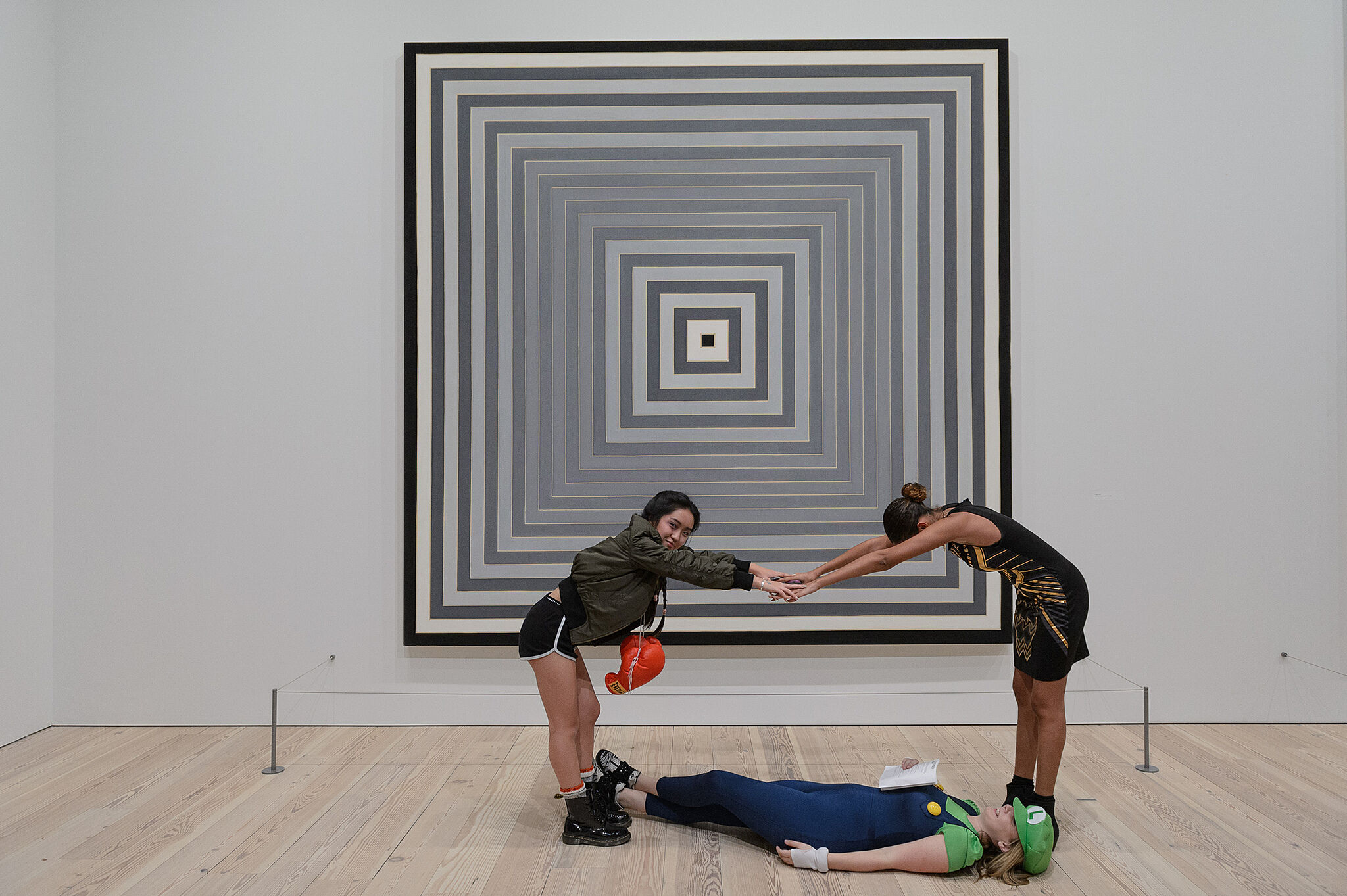 Three teens pose in front of a Frank Stella artwork.