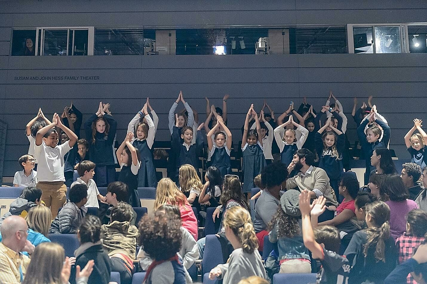 A group of students hold their hands over their heads in the audience.