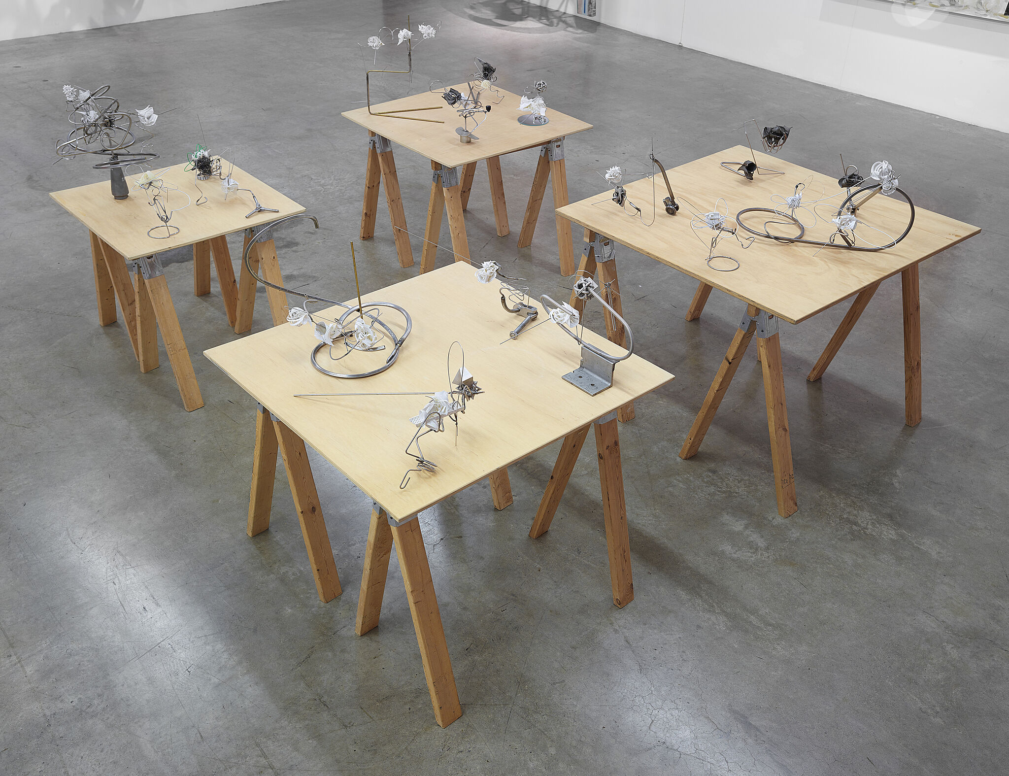 An installation of small metal sculptures on four wooden tables.