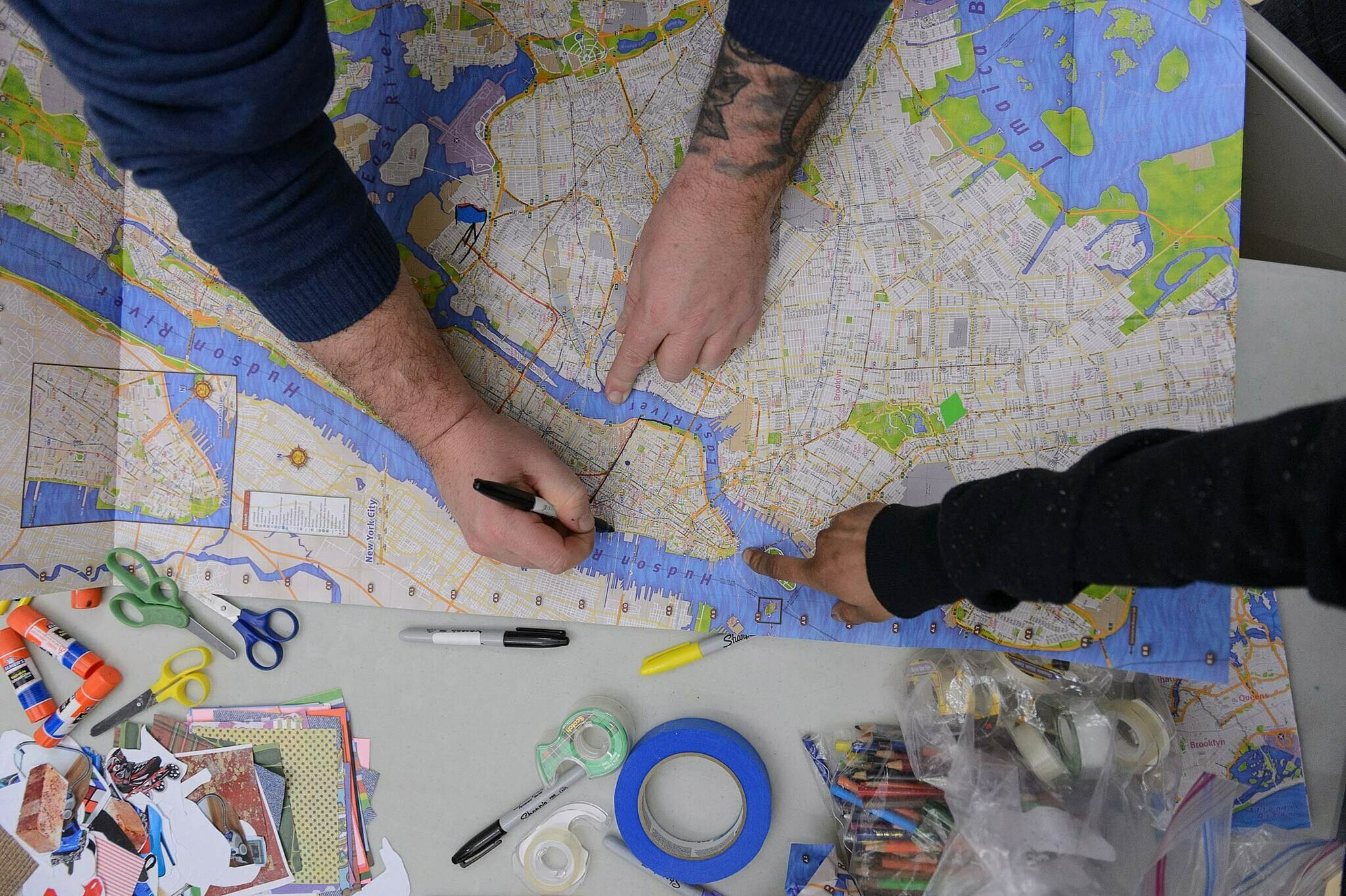 People drawing on a map with markers, with scissors, tape, and other materials on a table.