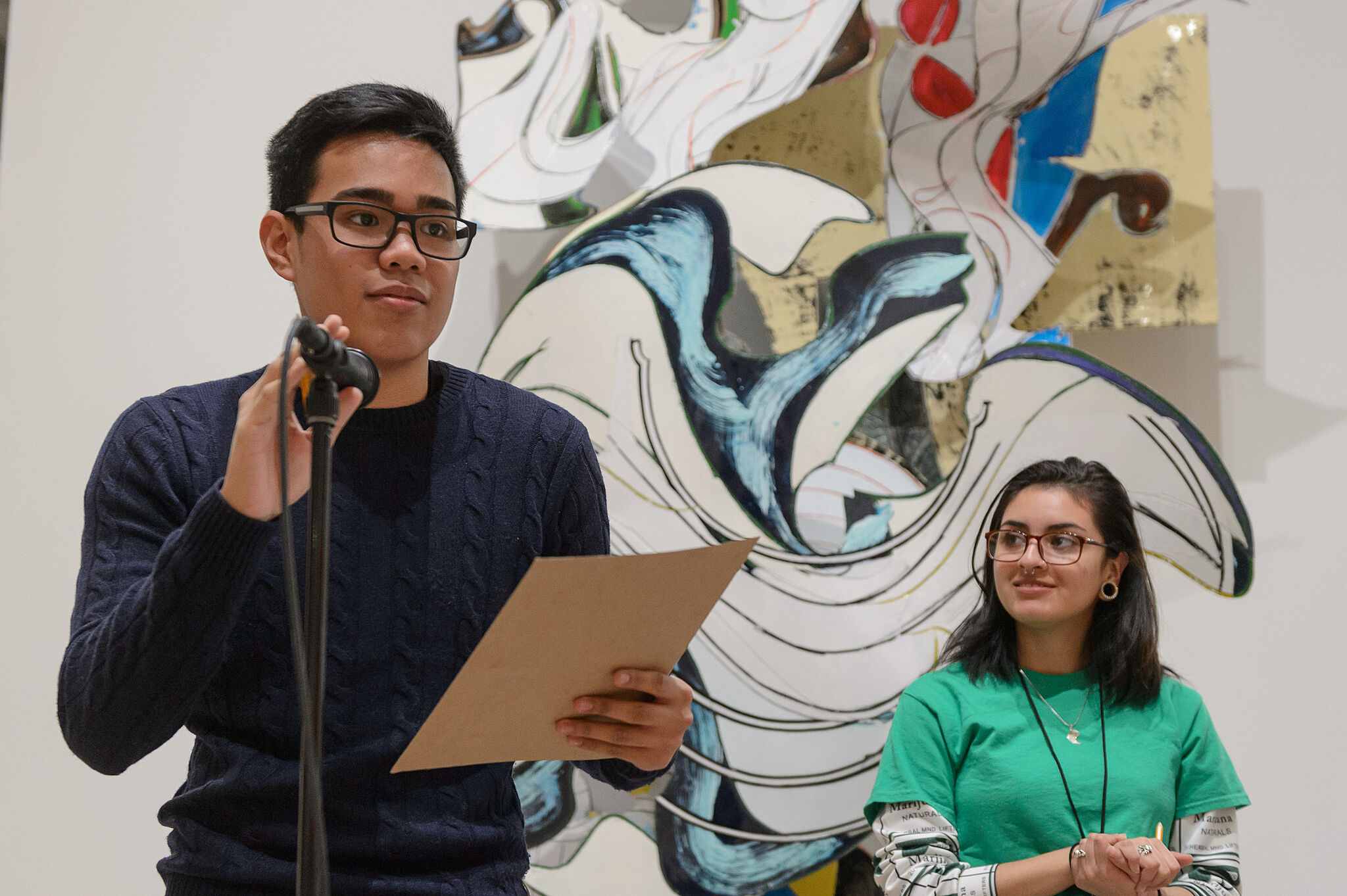 A student holds a microphone in front art by Frank Stella. 