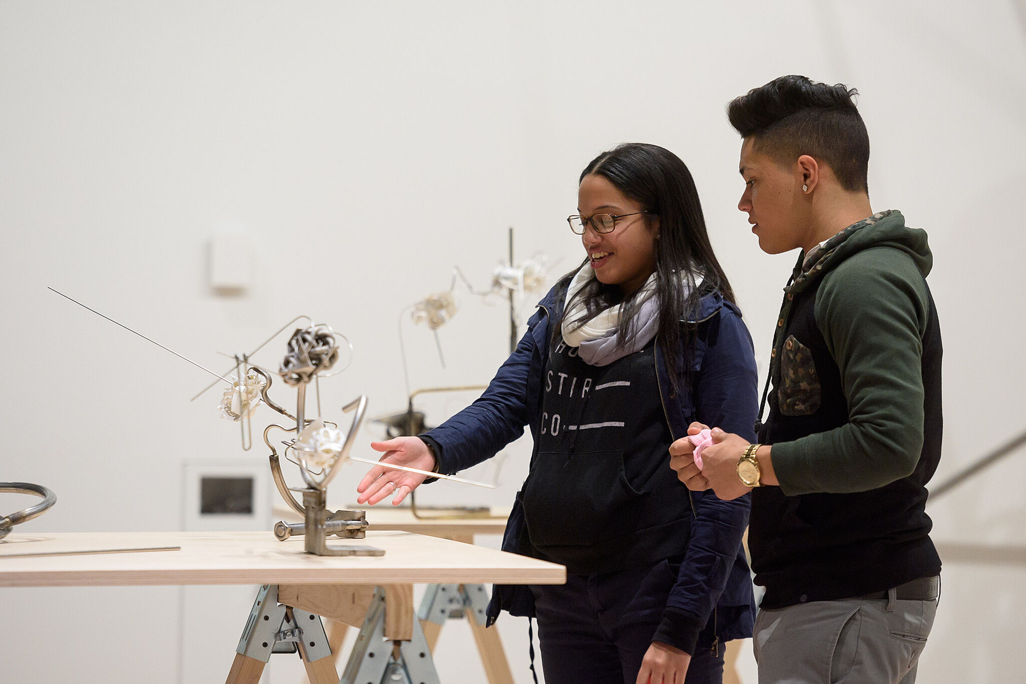 Two teens look at a sculpture on a table.