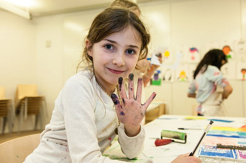 A girl holds up her fingers covered in paint