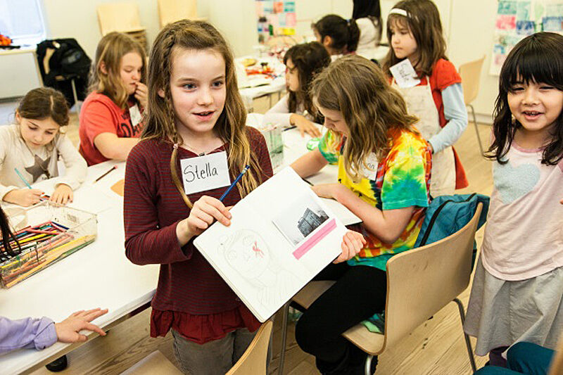 A child shows her work surrounded by other kids