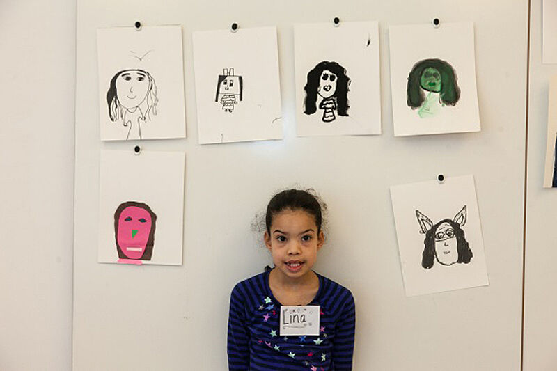 A girl stands next to student self-portraits