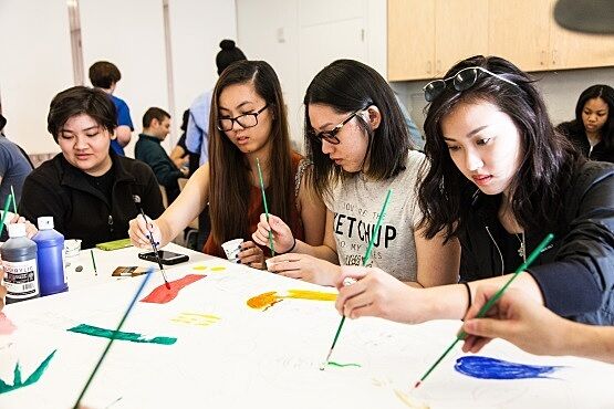 Students use paint brushes to create art on paper.