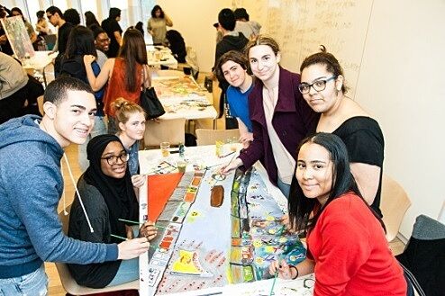 A table of students smiles while they make a painting together.