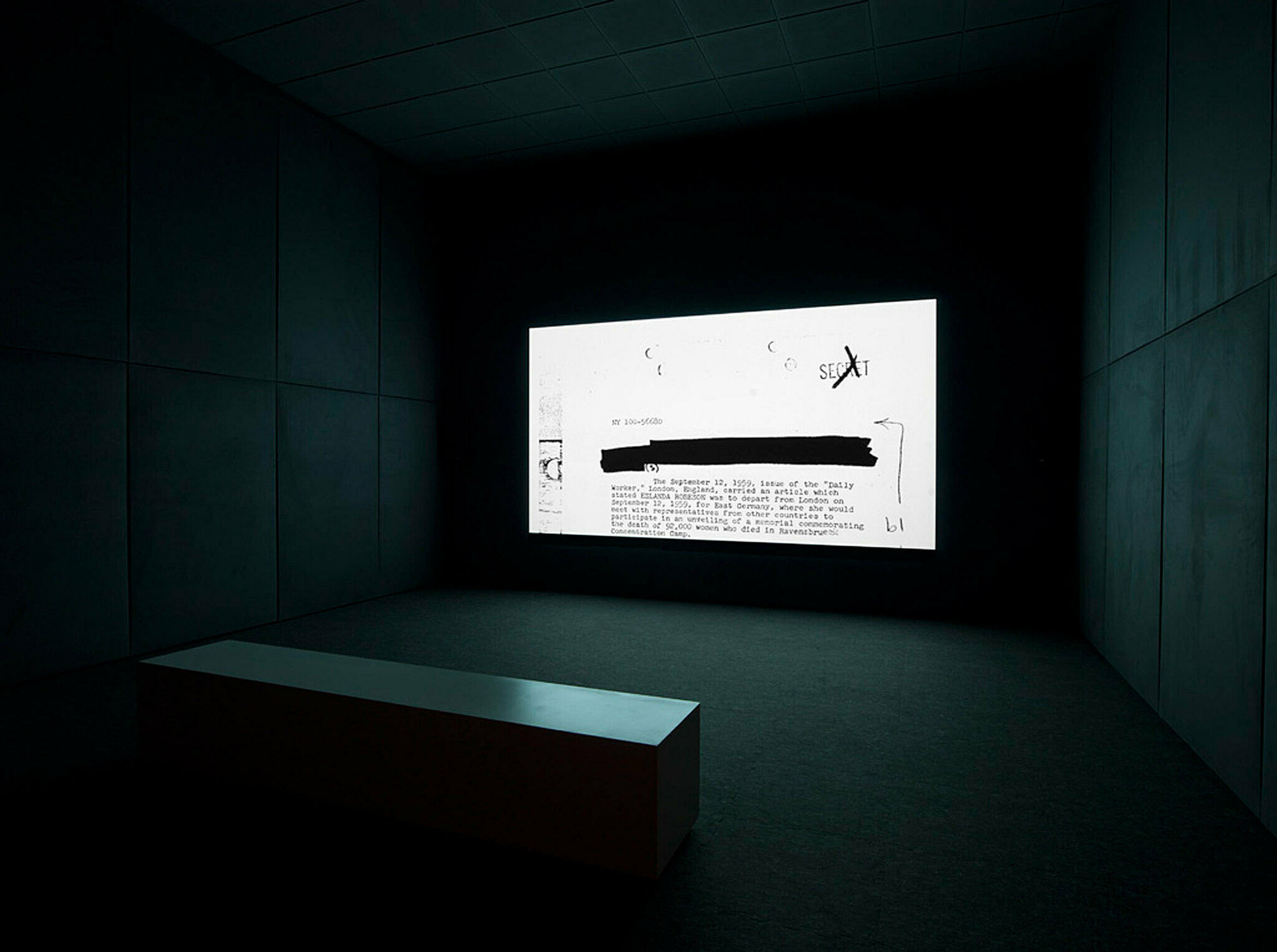 A projection of a work by Steve McQueen. A typed document flickers on the screen in a dark gallery