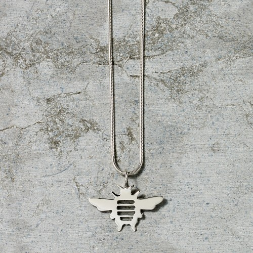 Silver necklace with a bee-shaped pendant on a textured concrete background.