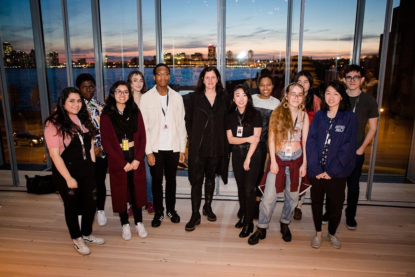 A group of teens poses with filmmaker Laura Poitras in a gallery overlooking the Hudson River.