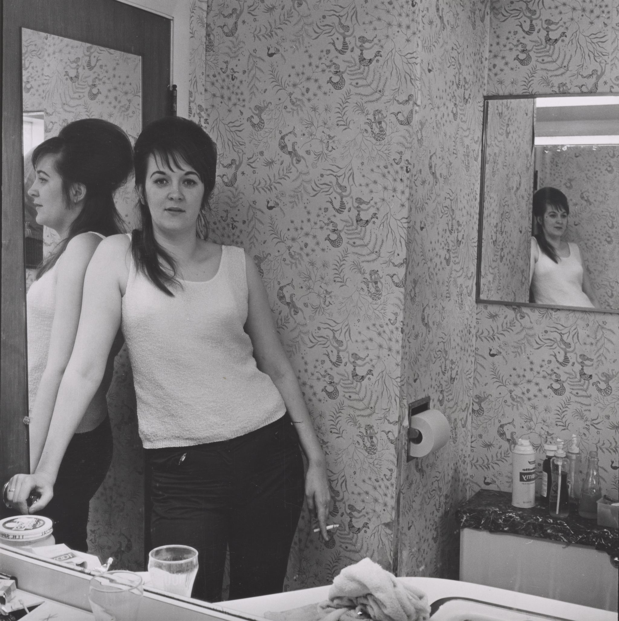A photograph of a woman standing in a bathroom.