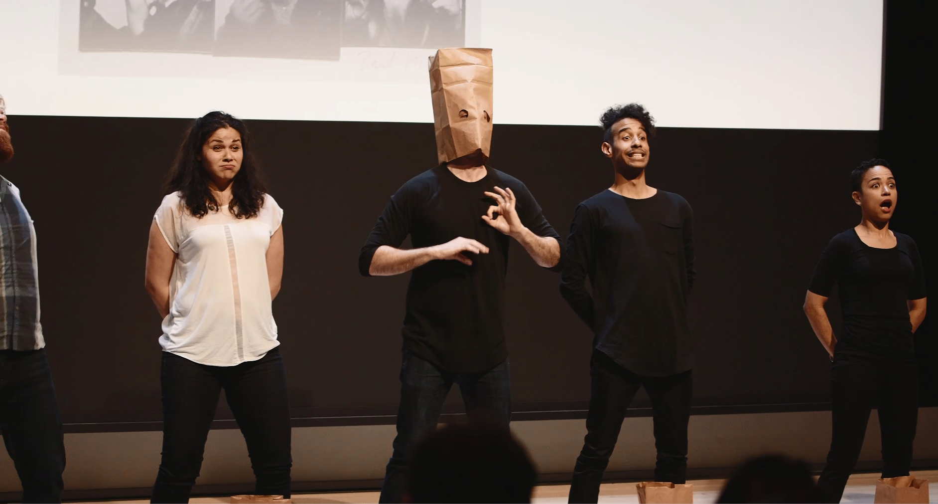 A performer wears a paper bag with two other performers on either side