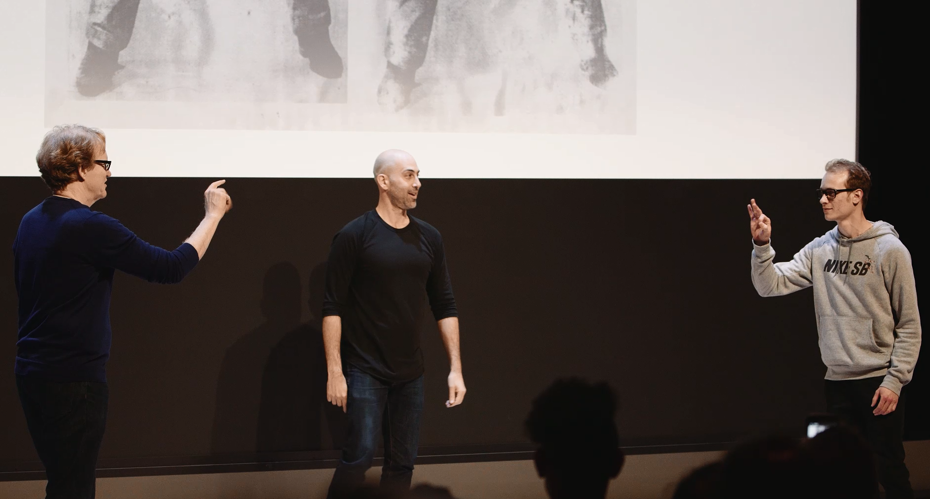 Two men sign towards each other while another stands between the two, judging.