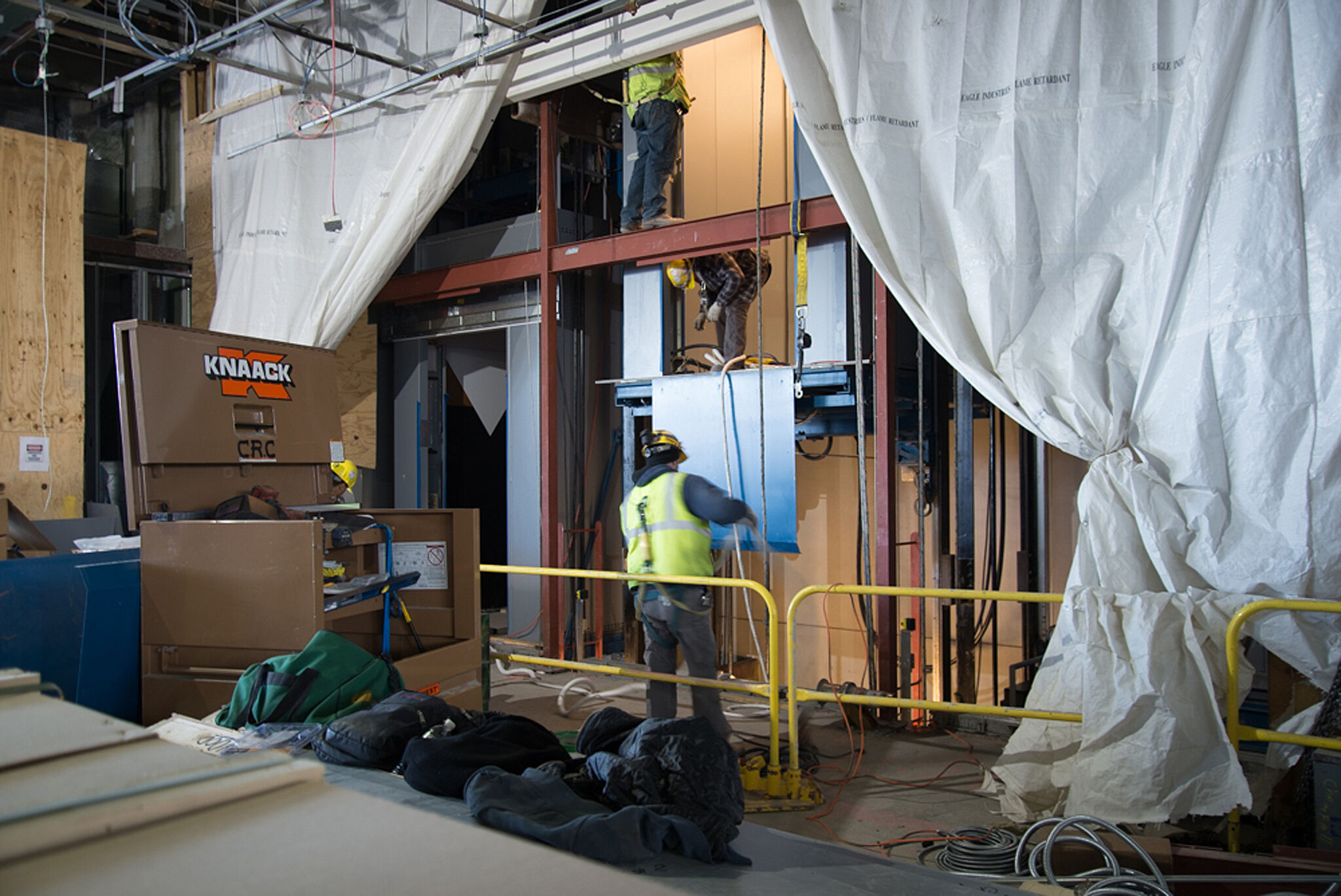Construction workers wearing safety gear work on a large elevator.