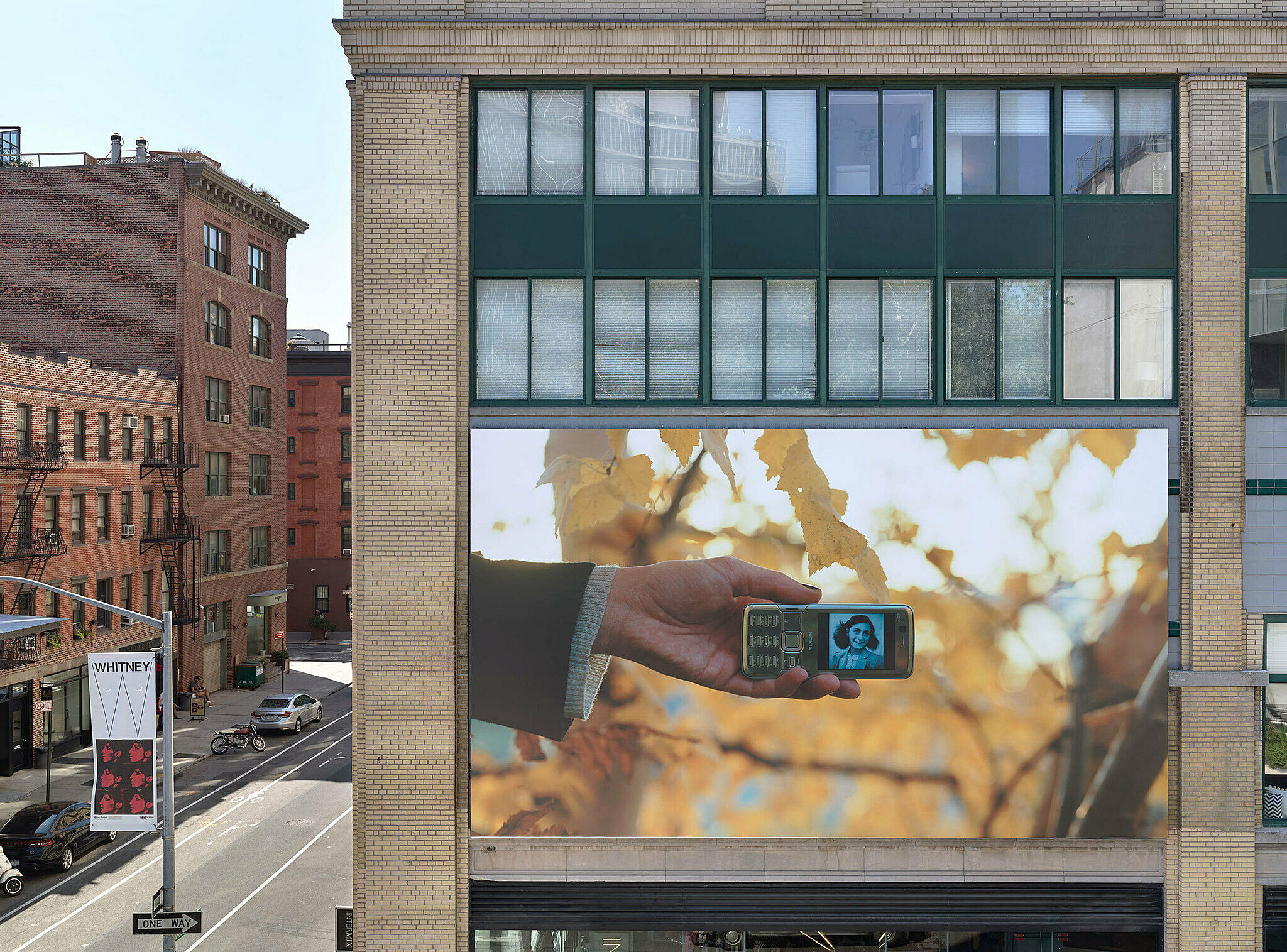 A hand holds a smartphone where a portrait of Anne Frank appears