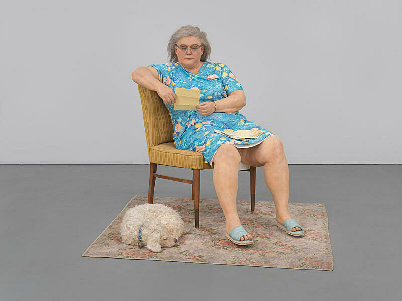 A sculpture of a woman reading on a chair next to a sleeping dog.