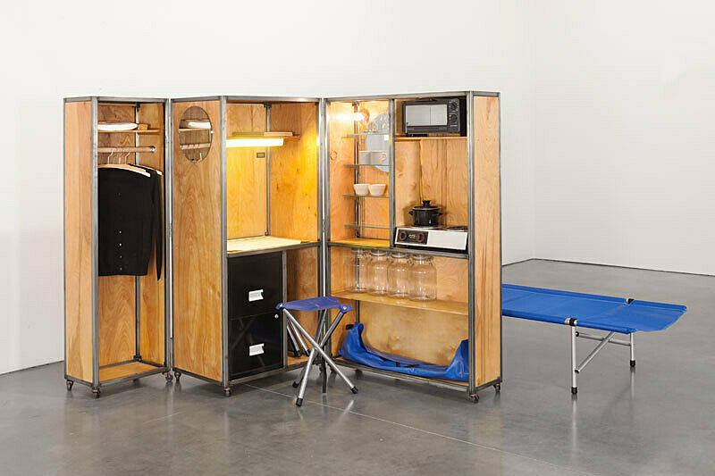 A sculpture of a small living unit that features clothes, cabinets, a stove, and other household items.