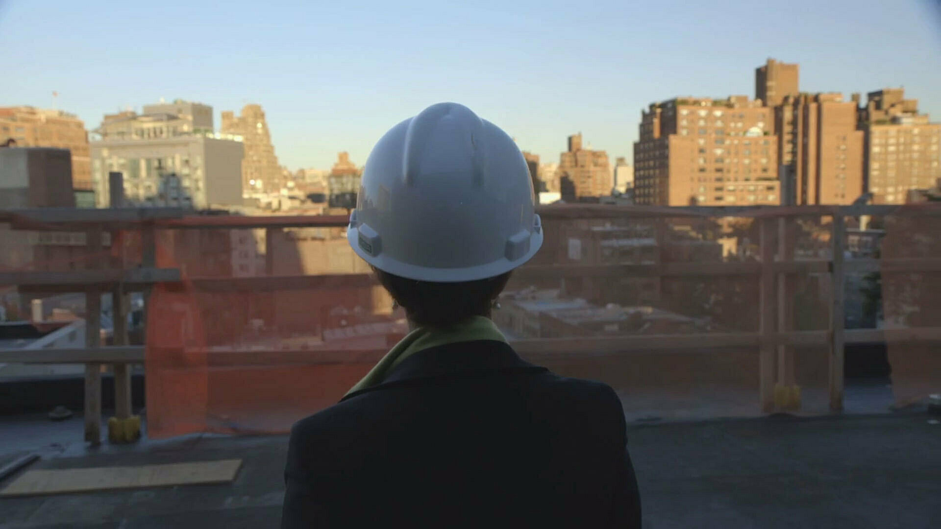 A woman in a hard hat, looking at the city skyline