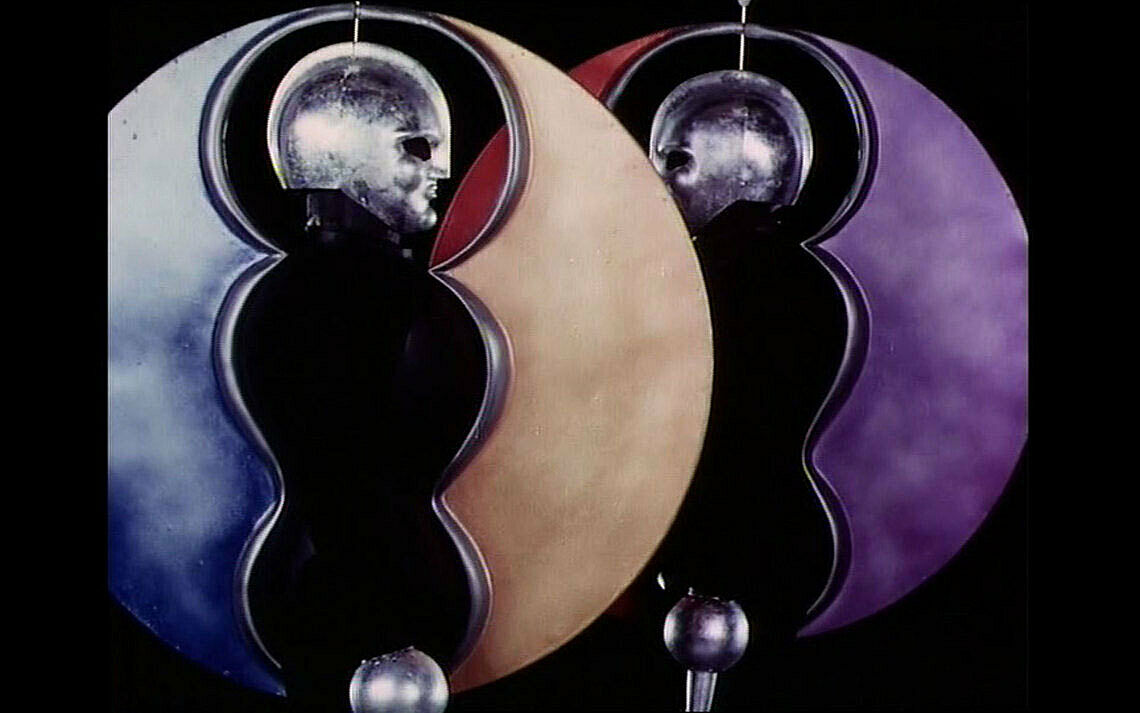 A still from a film created after Oskar Schlemmer. Two figures dressed in costume resemble Dadaist performers; both wear masks