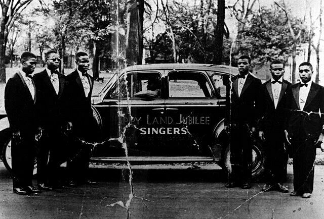 The Blind Boys of Alabama posed in front of a black car