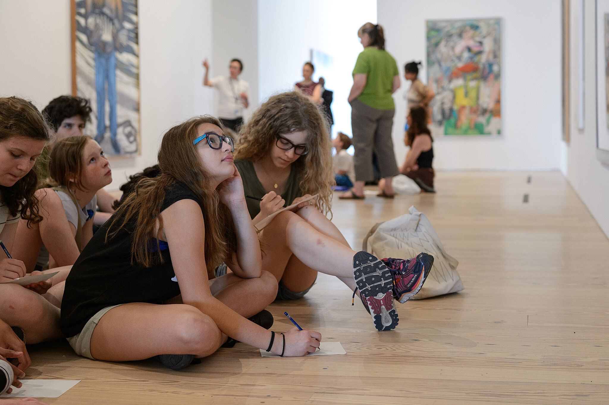 students sit looking up at artwork on gallery floor