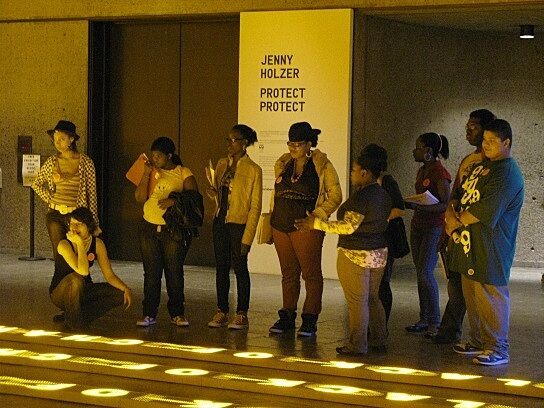 group of students stand in yellow hewn room