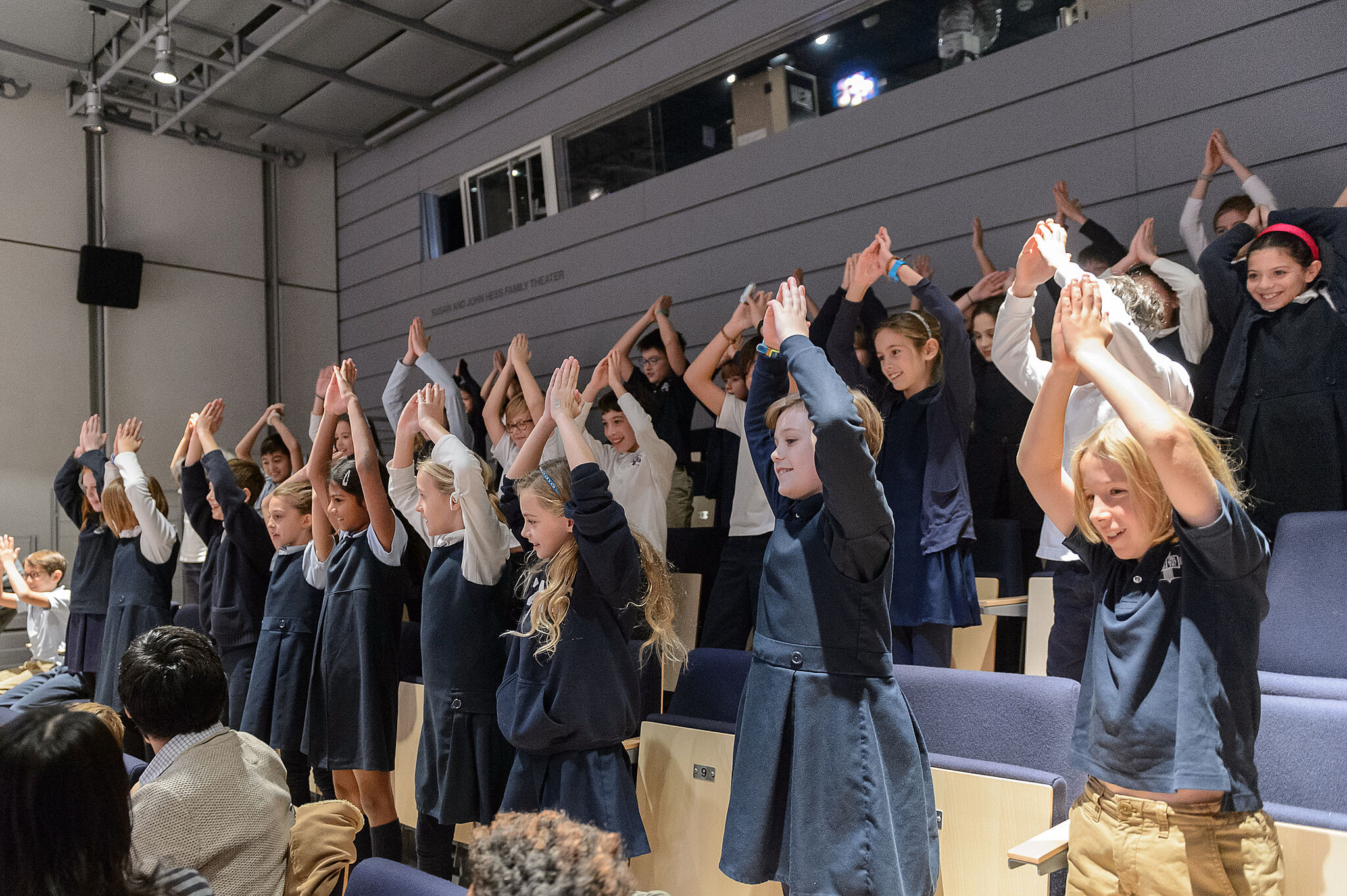 children holding up hands in auditorium