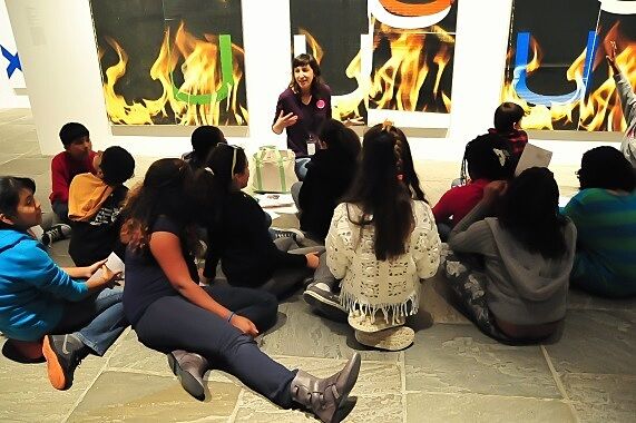 Students sitting on gallery floor in front of art.