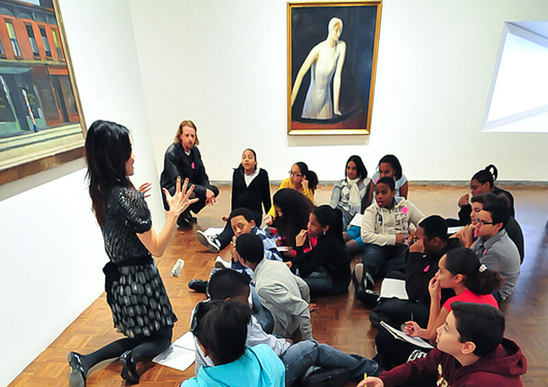 Educator sits up and explains in front of artwork.