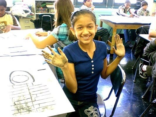 Girl with charcoals on hands holding up hands.