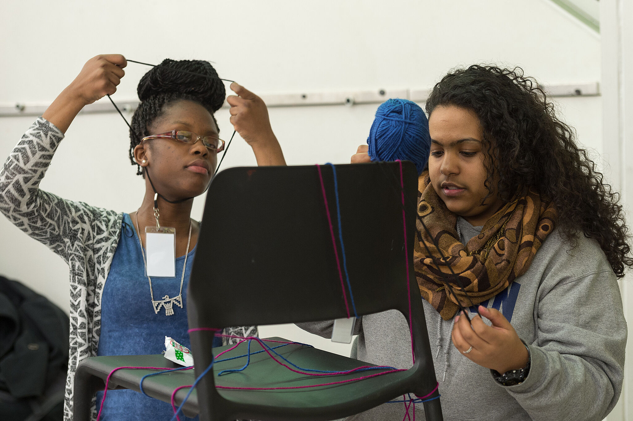 Two students use yarn and a chair to work on a project.