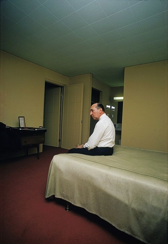 Man sitting on a bed in a room with red carpet.