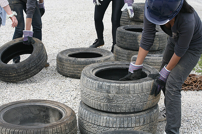 A worker grabs a tire from a pile on the ground.