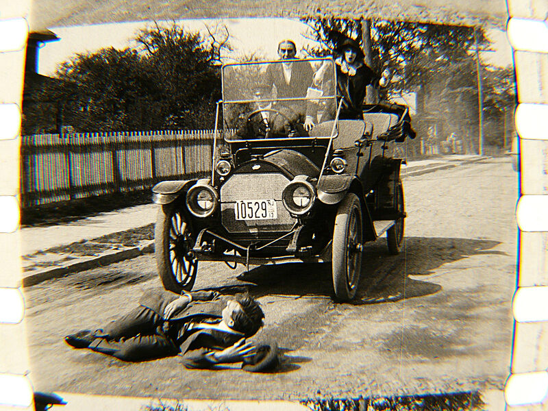 A man lies down in front of a car in the middle of the road.