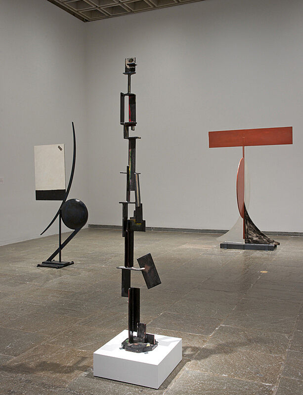 Three geometric sculptures stand in a gallery.