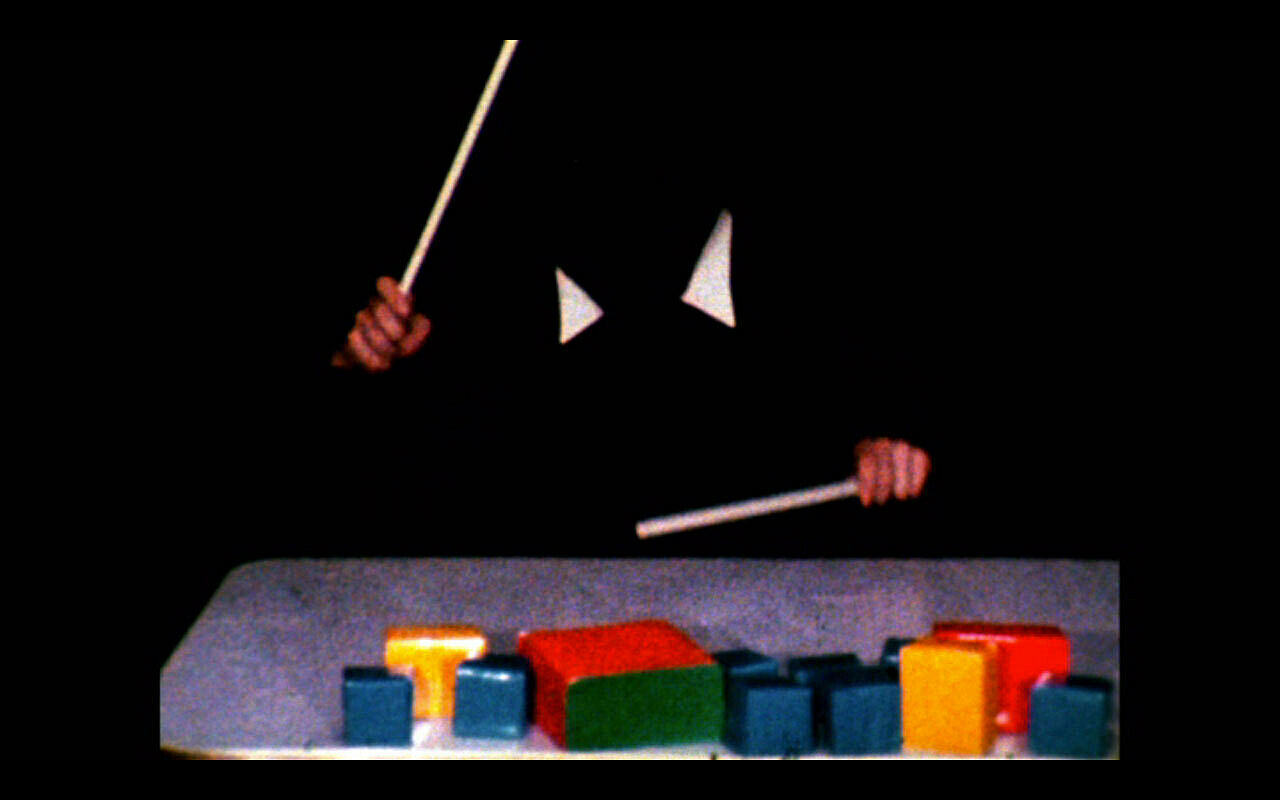 A video still of two hands holding drumsticks over a series of colored shapes.