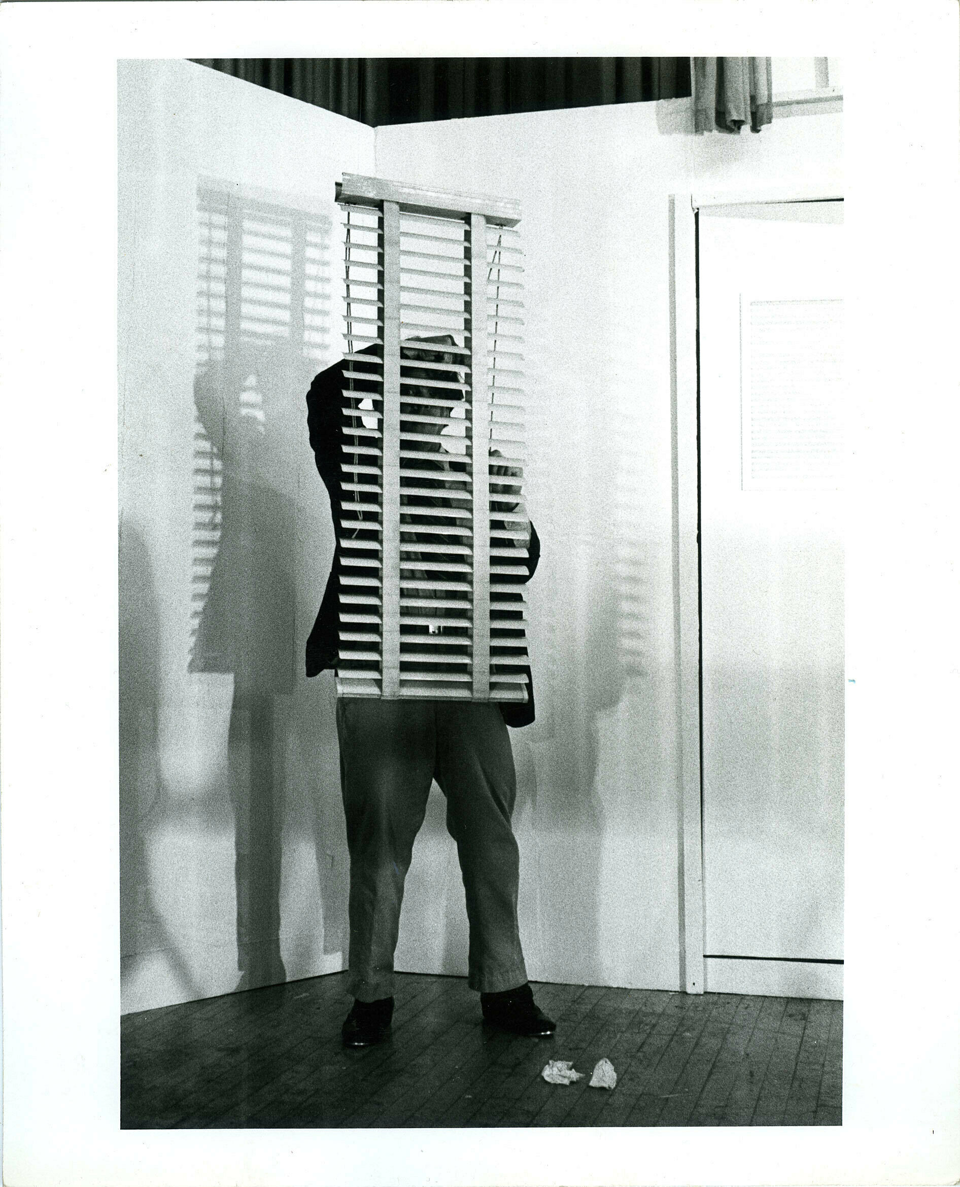A man stands behind window blinds that he is holding. 