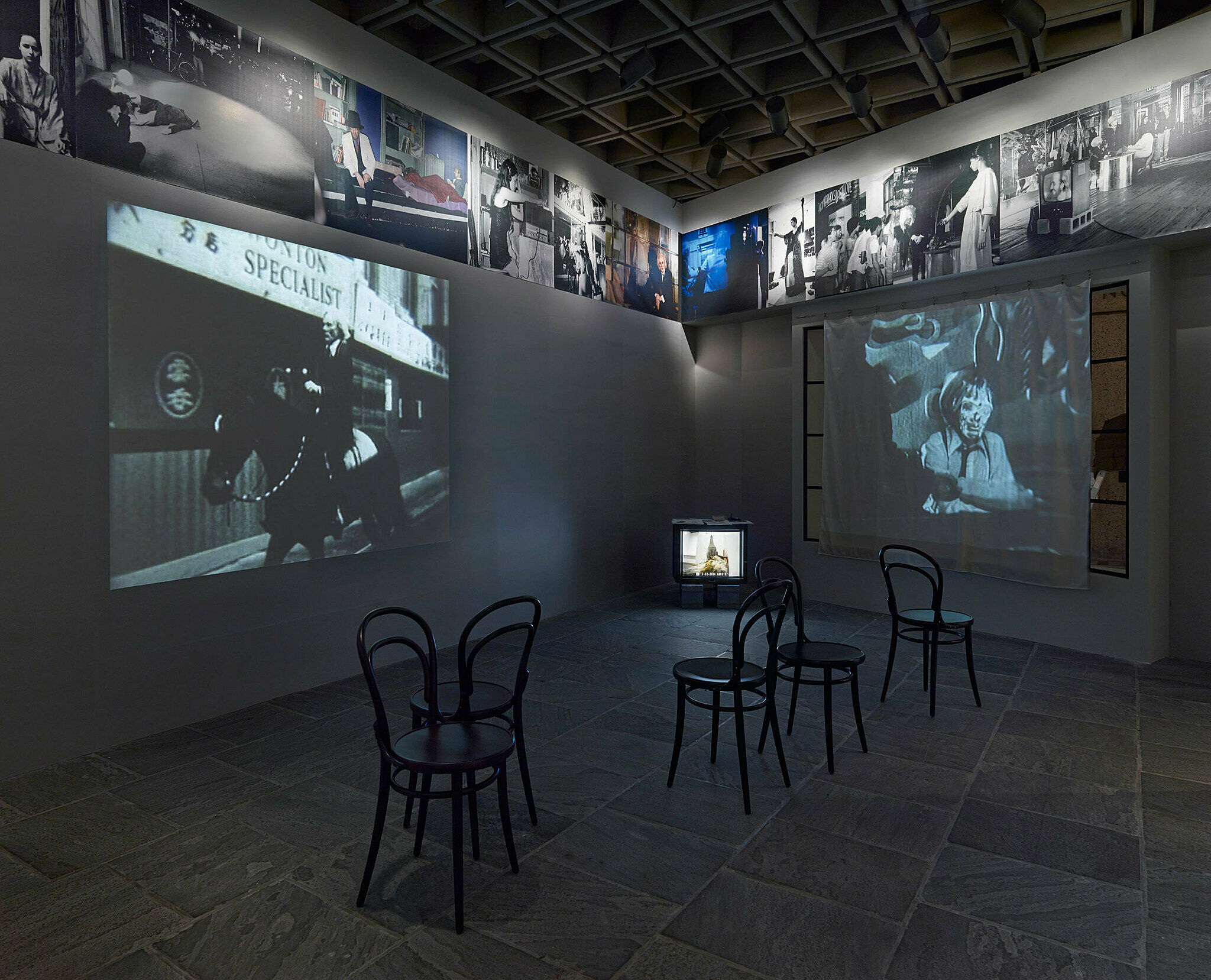 Art installation with chairs on the floor and television screens on two walls.