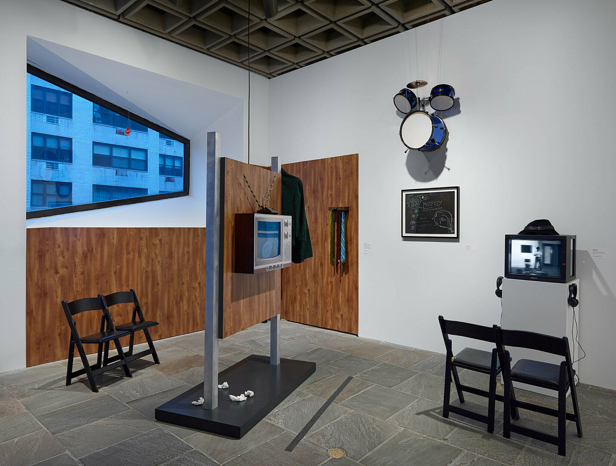 Art installation with two televisions drums hanging on the wall.