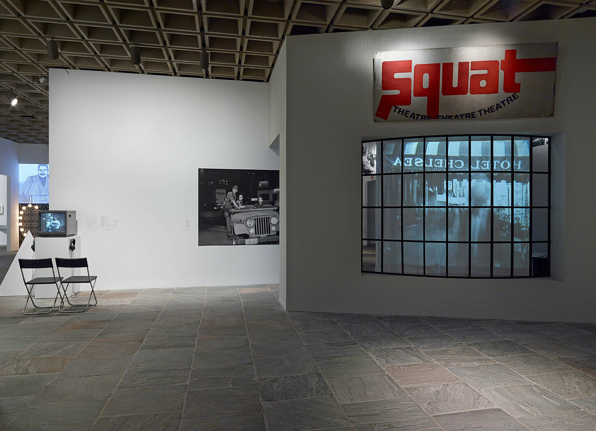Art installation in a gallery with a window, two chairs and photo on the wall.