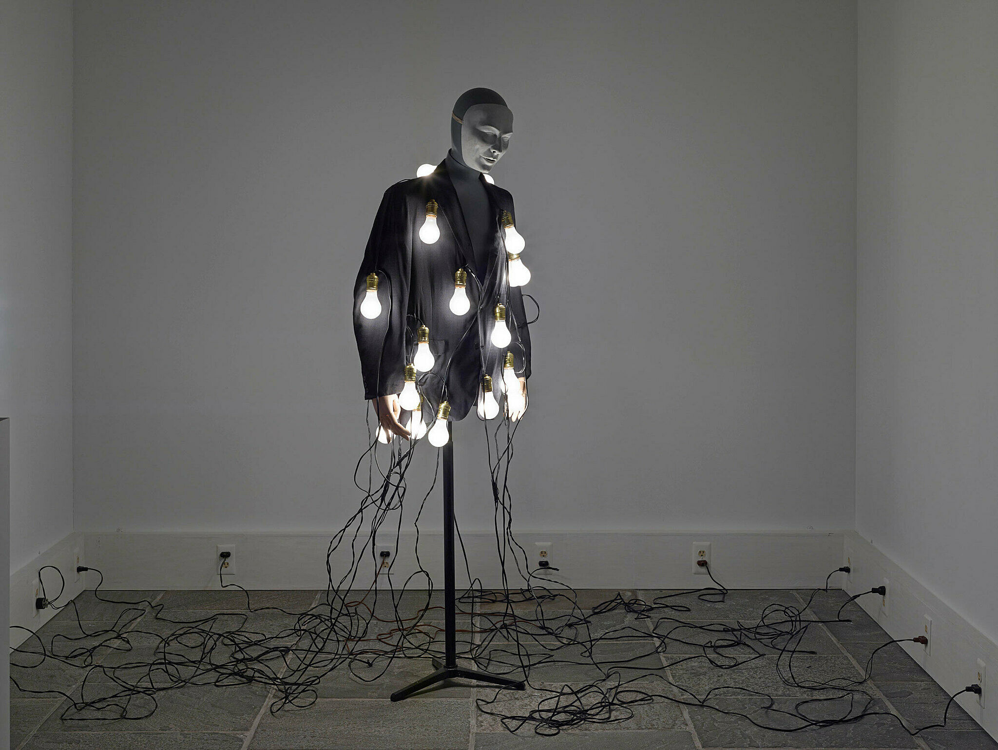 A mannequin covered in lightbulbs in the middle of a room.