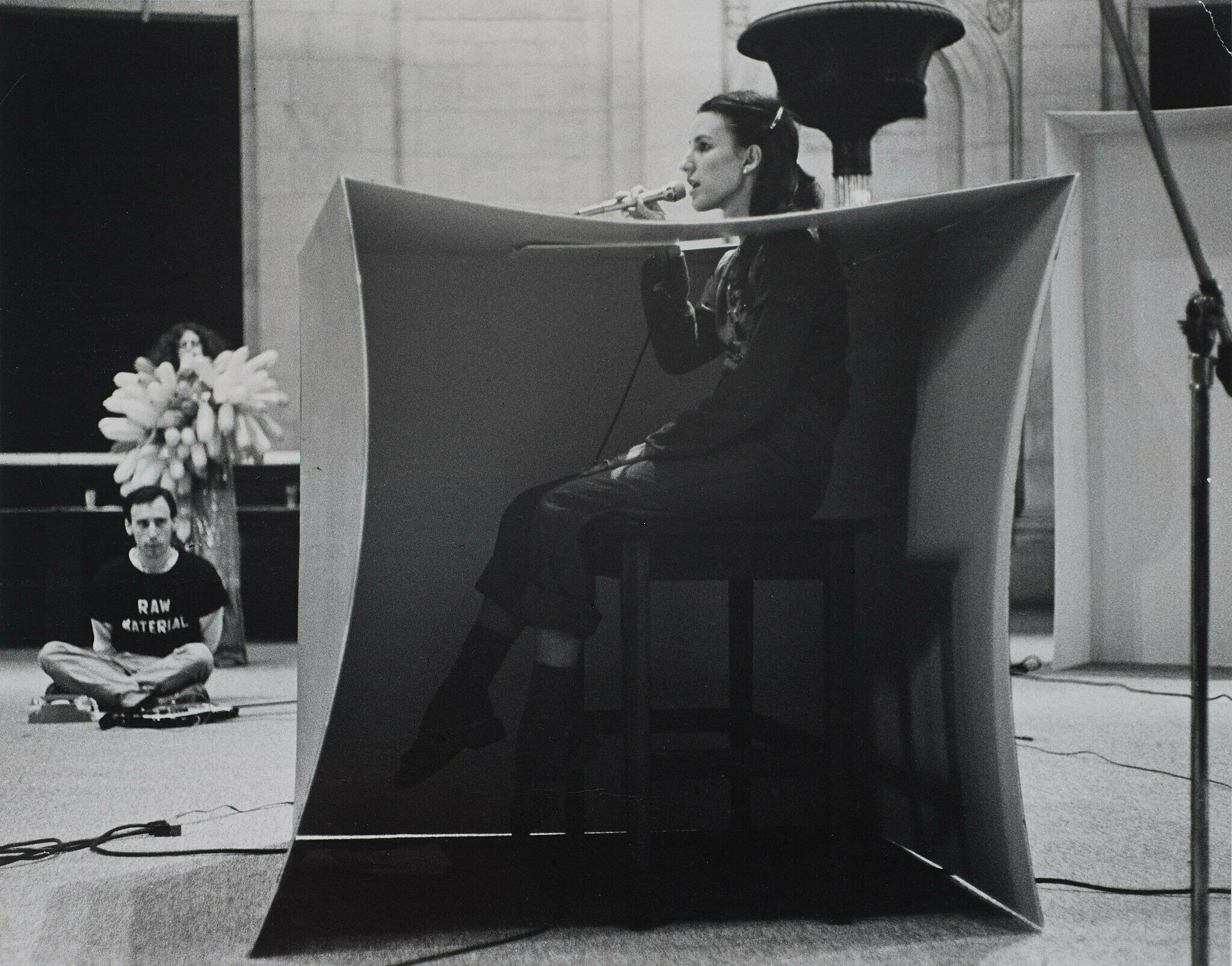 A woman holds a microphone to her mouth during a live art performance.