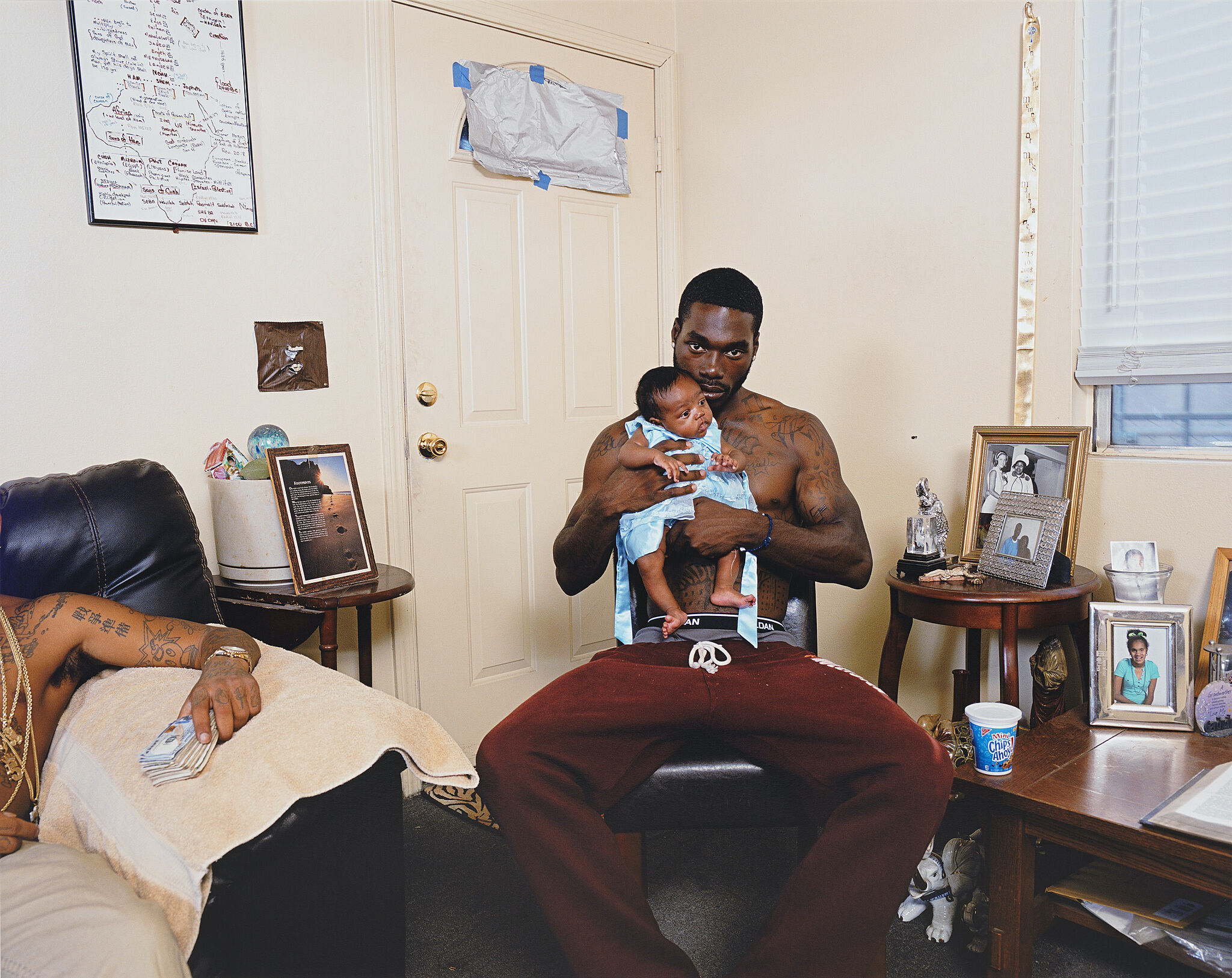 A photograph of a person sitting in a chair holding a baby in a house.