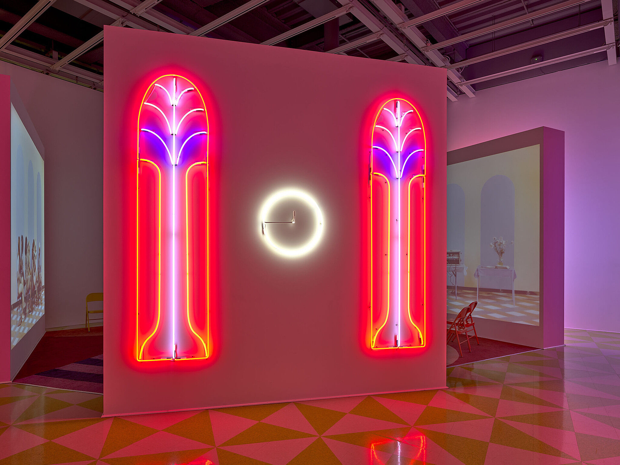 Two pink, purple and red Neon artworks with a yellow clock in the middle of them.
