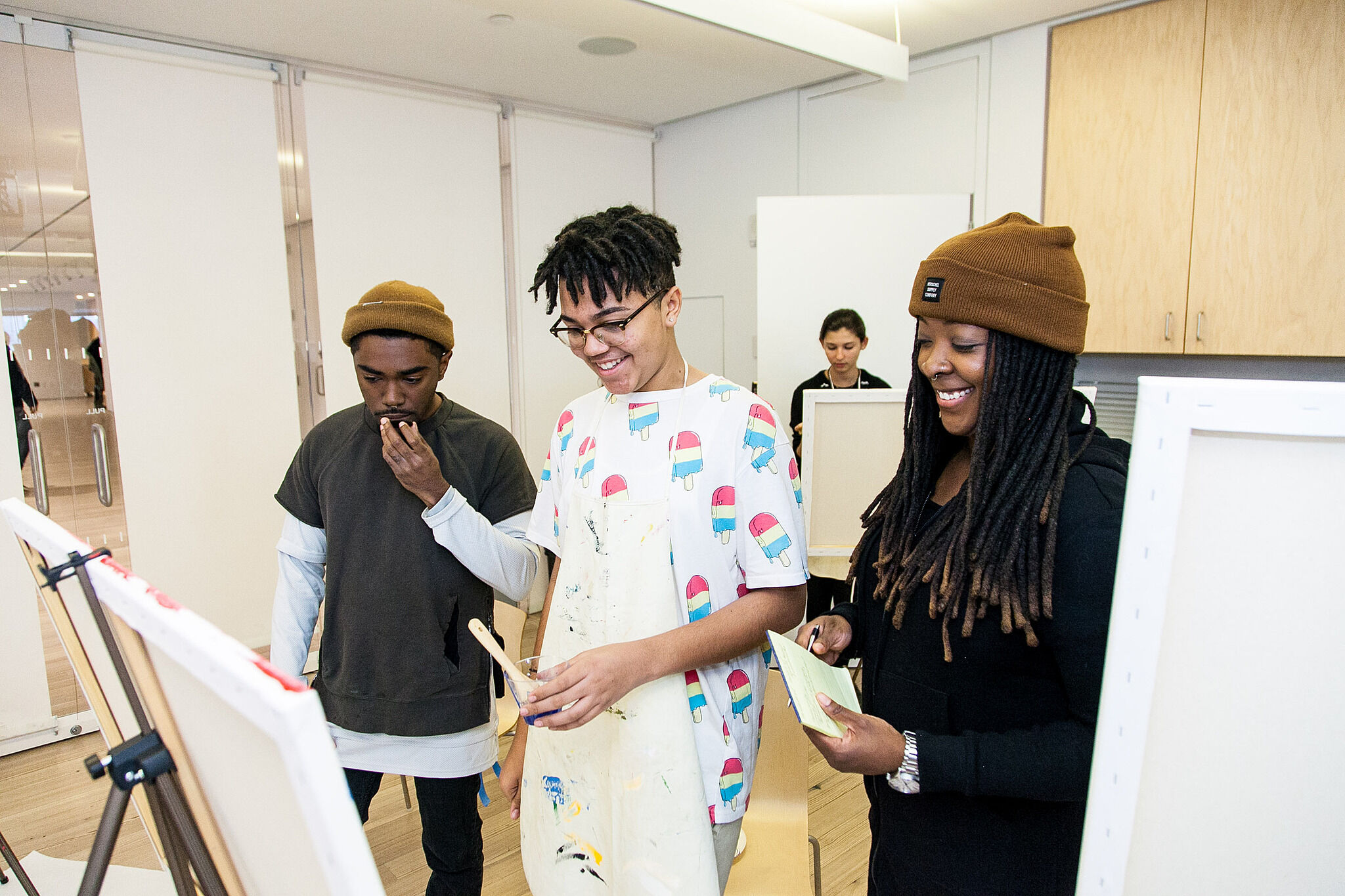 Artist and students stand in front of an easel.