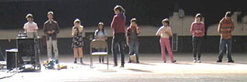 Students stand on a stage in front of teacher.